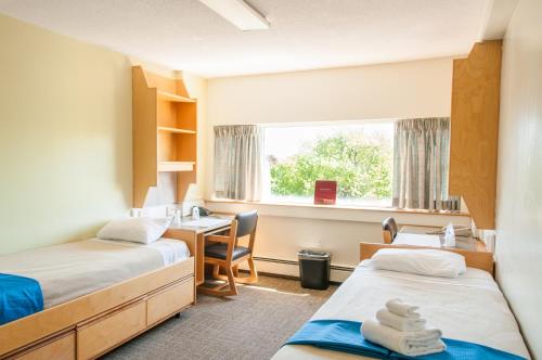 哈利法克斯圣玛丽大学会议服务及暑期住宿酒店的客房设有两张床、一张桌子和一个窗户。