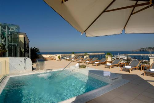伊斯基亚卡罗琳娜别墅酒店的庭院内一个带椅子和遮阳伞的游泳池