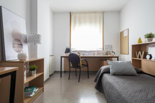 赫罗纳蒙蒂里维大学校园旅馆的一间卧室配有一张床和一张桌子及椅子