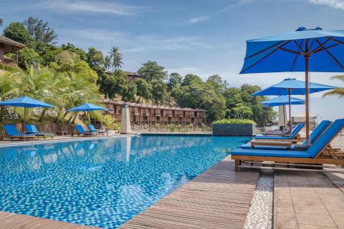 瑟古邦巴塔姆KTM假日酒店的度假村的游泳池,配有蓝色的椅子和遮阳伞