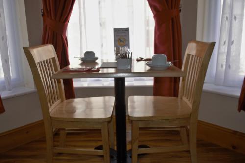 道格拉斯Sea Breeze Guest House的一张木桌、两把椅子、一张桌子和两个窗户