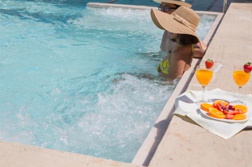 奥里安特隐修之地水疗酒店的坐在游泳池旁的一位戴帽子的女人,喝着饮料