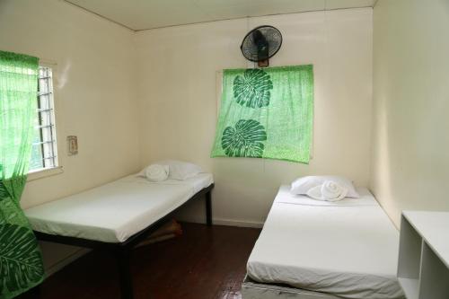 Vaitele萨摩亚度假屋的小房间设有两张床,配有绿色窗帘