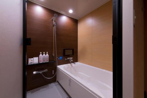 东京The CALM Hotel Tokyo的一间带浴缸和淋浴的浴室,拥有木墙
