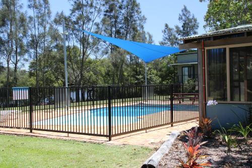 Wooli乌利河度假屋的铁栅围着一个游泳池,上面有蓝色的油布