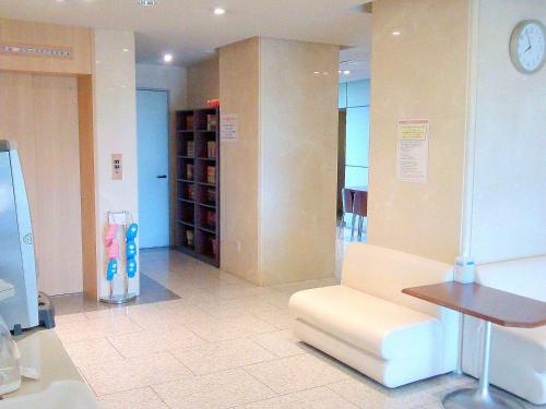 Okaya冈谷市中央大酒店 的一间设有白色沙发和时钟的等候室
