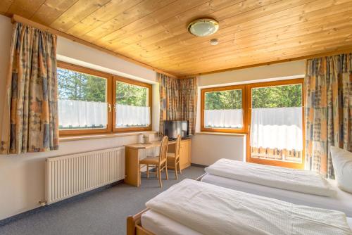 圣安东阿尔贝格Pension Sattelkopf的一间卧室配有两张床、一张桌子和两个窗户。