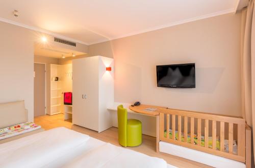路茨曼贝格全红蓝酒店的一间卧室配有婴儿床,墙上配有电视。