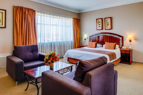 布拉瓦约Bulawayo Rainbow Hotel的酒店客房配有一张床、两把椅子和一张桌子