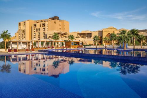 利雅德InterContinental Durrat Al Riyadh Resort & Spa, an IHG Hotel的一个带棕榈树和建筑的游泳池的度假酒店