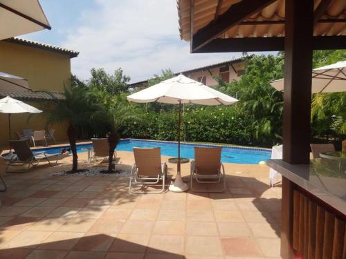 普拉亚多Condomínio Solar dos Peixes的一个带椅子和遮阳伞的庭院和一个游泳池