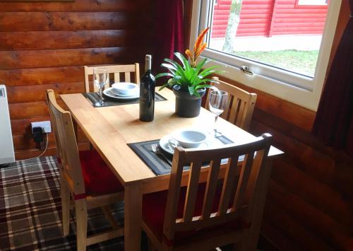 达农Pucks Glen Lodges, Rashfield, by Dunoon的一张木桌,上面放着一瓶葡萄酒和一株植物