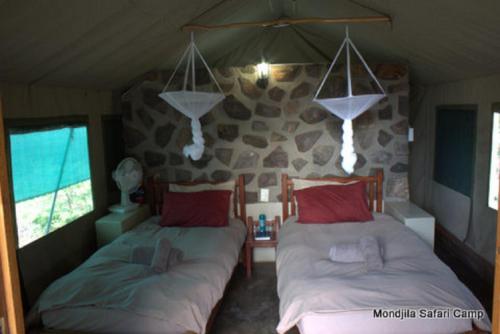 奥考奎约Mondjila Safari Camp的一间卧室设有两张床和石墙