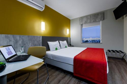 库里提巴Go Inn Hotel Curitiba的酒店客房配有一张床铺和一张书桌上的笔记本电脑