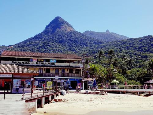 阿布拉奥Beira Mar Hostel & Suítes的海滩上的一座建筑,背景是一座山