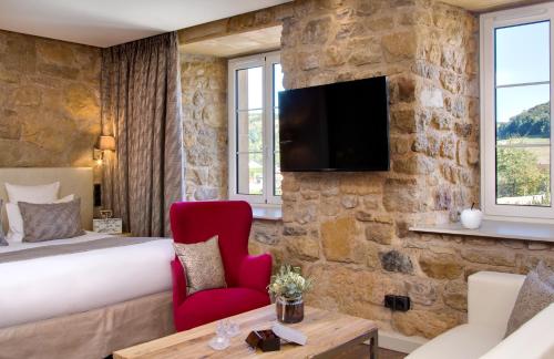 MontenachDomaine de la Klauss & Spa, Restaurant Gastronomique Le K的酒店客房,设有一张床铺和一台石墙电视