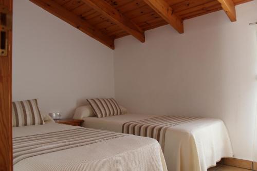 泰拜尔盖马辛旅舍的配有白色墙壁和木制天花板的客房内的两张床