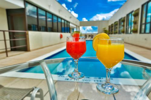 塔瓜汀加塔瓜汀加康福特酒店的坐在泳池旁的桌子上,三杯鸡尾酒