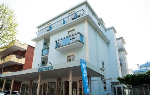 里米尼Hotel Ramona的前面有蓝色标志的白色建筑