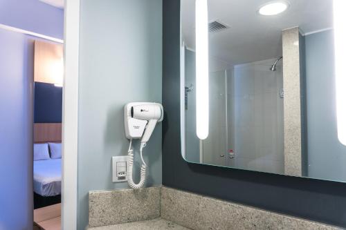 里约热内卢ibis Rio Porto Atlantico的浴室的墙上有一部电话,旁边是镜子