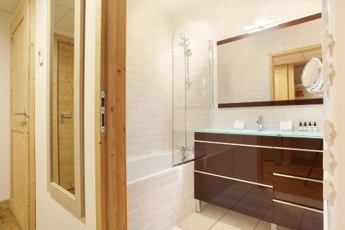 拉克吕萨Hôtel Prestige Odalys Le Chamois的带浴缸、水槽和镜子的浴室