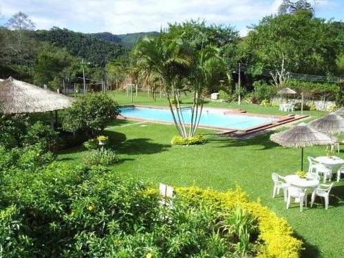 Morro AzulParque Hotel Morro Azul - a 12 km do Parque dos Dinossauros的花园设有游泳池、桌子和遮阳伞