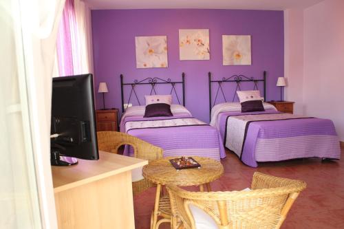 TalaveruelaHostal Zaguan的紫色的客房配有两张床和一张桌子及一台电视机