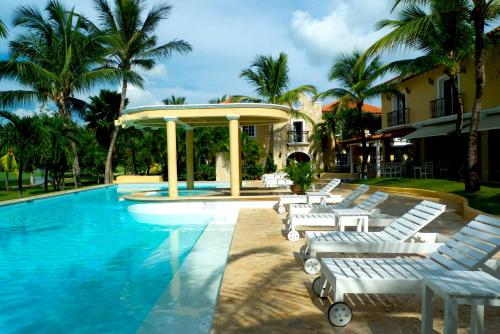 蓬塔卡纳高尔夫套房酒店的一座带白色躺椅的游泳池,位于大楼旁