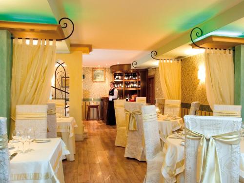 瓦尔纳首都酒店的一间设有白色桌椅的餐厅,以及一名女服务员