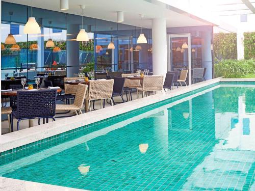 里约热内卢诺富特里约热内卢奥林匹克公园酒店的餐厅旁的游泳池配有桌椅