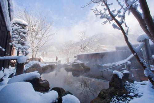 高山Miyama Ouan Kyoritsu Resort的一座建筑物旁边一个被雪覆盖的池塘