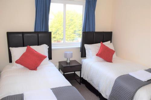 福尔柯克Kelpies Serviced Apartments Alexander- 2 Bedrooms的一间卧室配有两张带红色枕头的床和窗户。