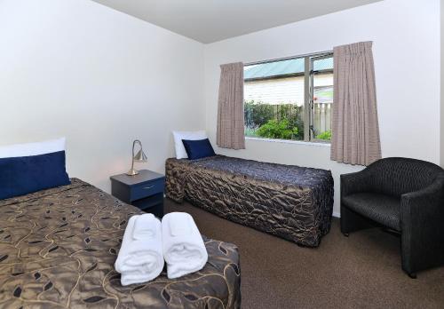 基督城竞技场汽车旅馆的一间卧室设有两张床、一把椅子和一个窗户。