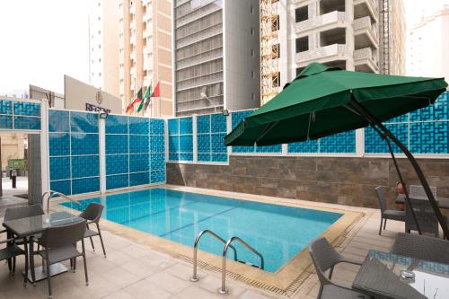 科威特勒金特公寓式酒店的一个带桌椅的游泳池和一个绿色遮阳伞