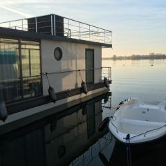 Modernes festliegendes Hausboot mit großzügiger Dachterrasse und Ruderboot